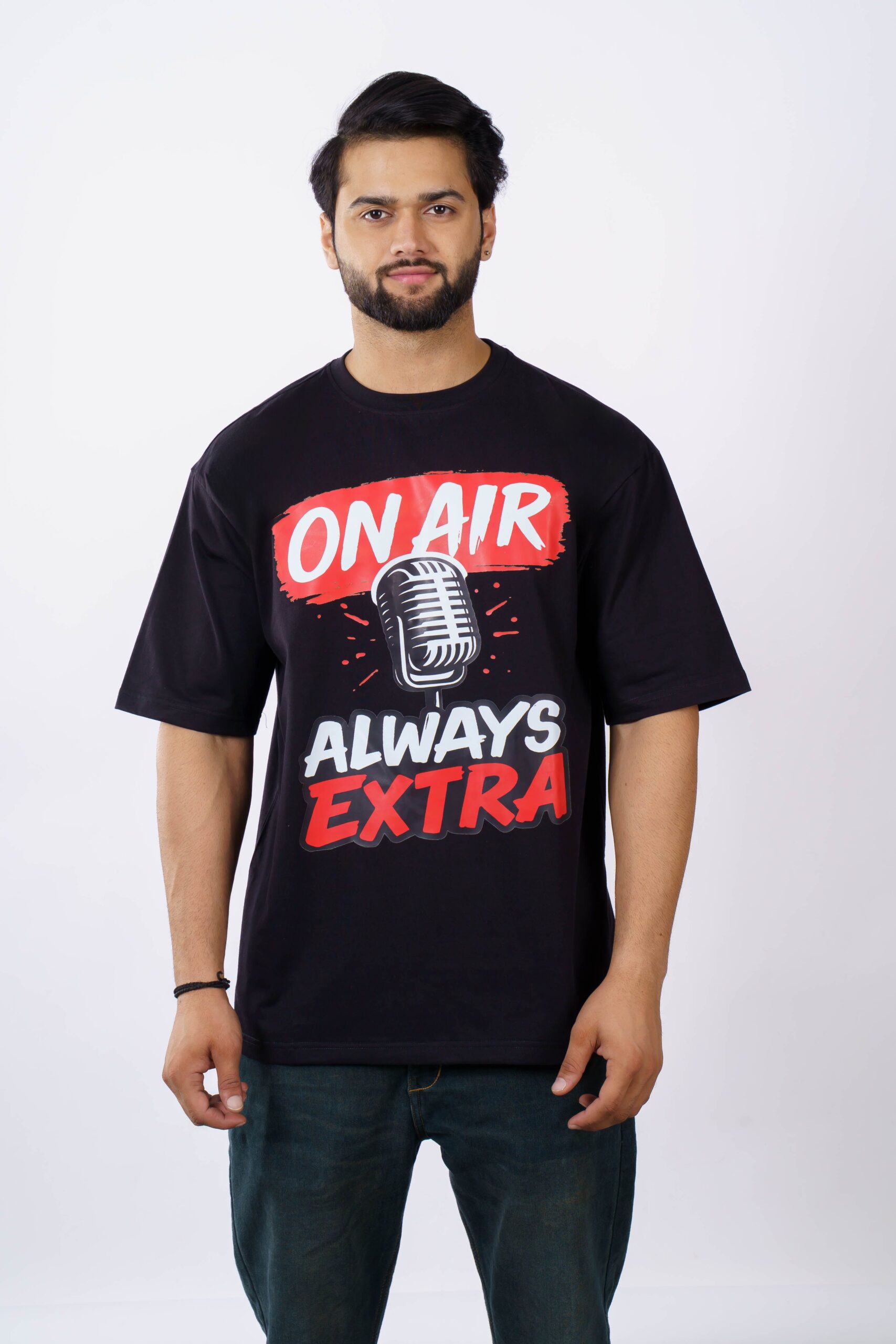 Young man in Delhi wearing an oversized black t-shirt with 'On Air Always Extra' printed, studio shot.